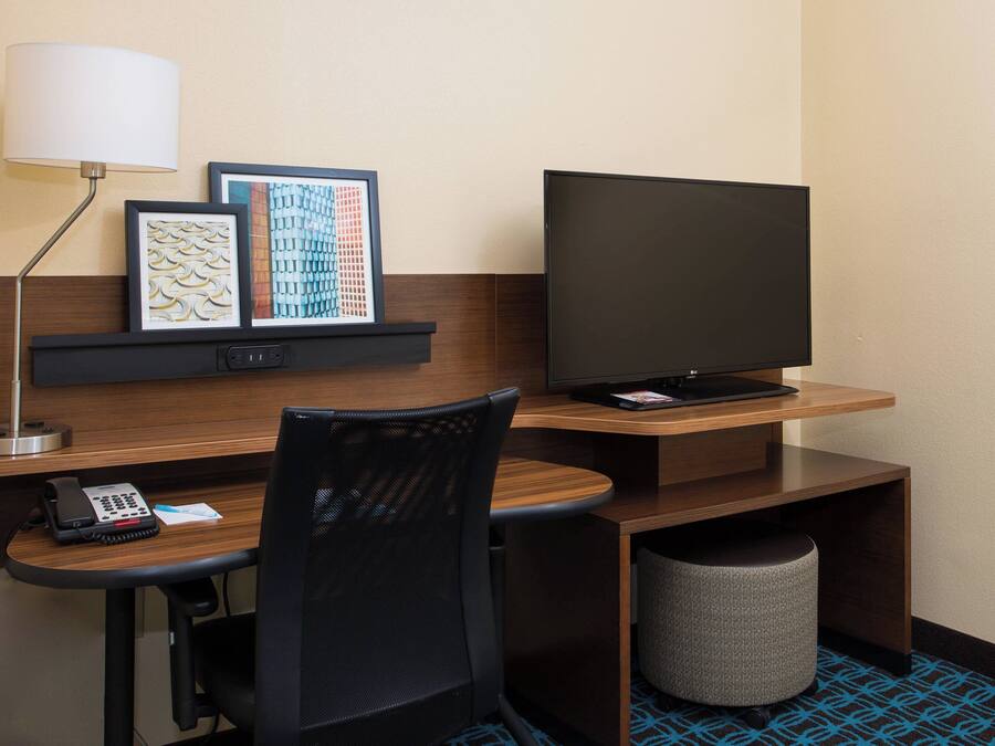 A hotel room with a desk, a chair, a television, a lamp, and a waste bin.