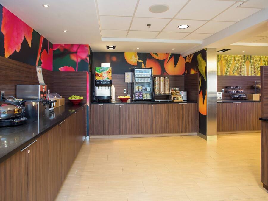 A modern kitchen with wooden cabinets, a stainless steel refrigerator, and a fruit display.