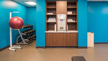 A gym with exercise equipment, a hydration station, and a bench.