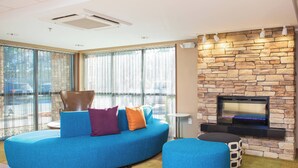 A modern living room with a blue sofa, ottoman, and a stone fireplace. - Fairfield by Marriott Inn & Suites Raynham Middleborough/Plymouth (Middleborough)
