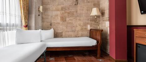 A small, cozy room with a single bed, a wooden nightstand, a wall-mounted TV, and a stone wall.