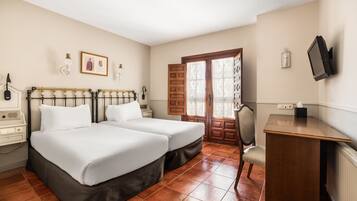 A hotel room with two beds, a desk, a chair, a television, and a window with a view of the outside.