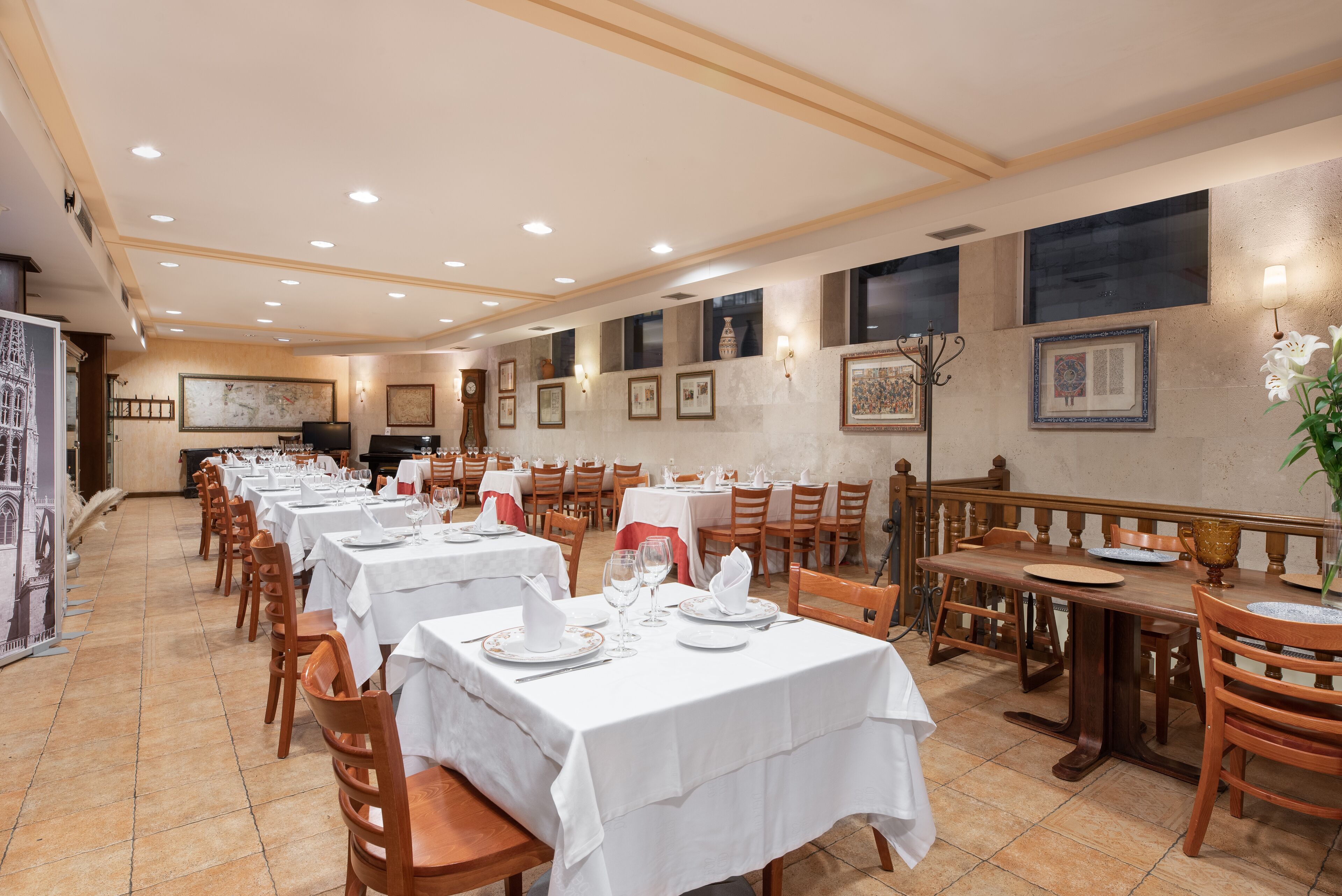 A restaurant with multiple tables set for dining, featuring white tablecloths and wooden chairs.