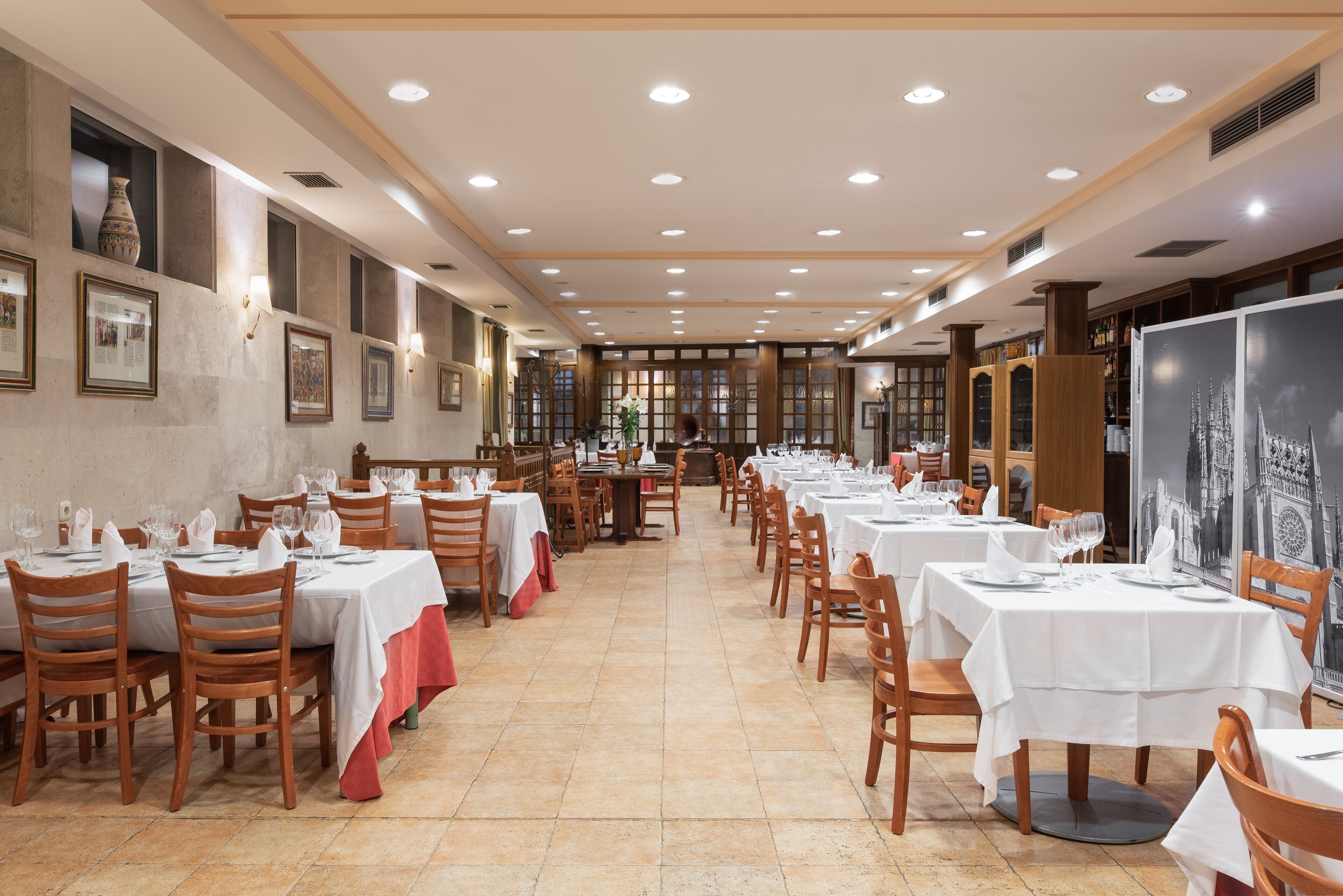 A spacious dining area with multiple tables and chairs, a tiled floor, and framed artwork on the walls.