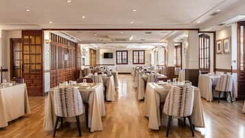 Een ruime hotel eetzaal met meerdere tafels en stoelen, houten vloer en een centrale gang.