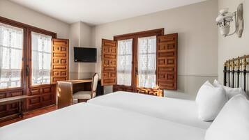 A hotel room with a large bed, wooden wardrobe, desk, chair, and a TV on the wall.