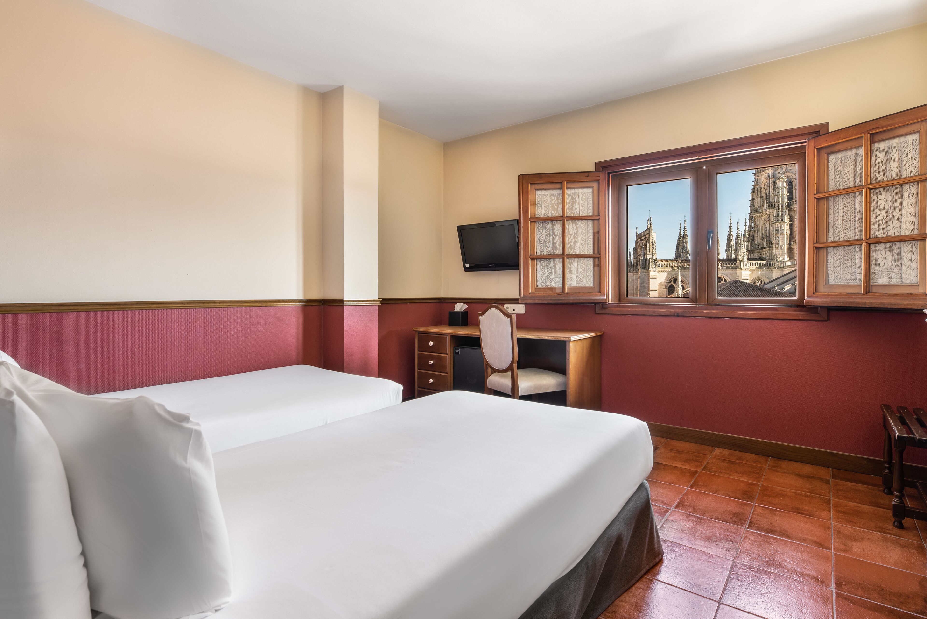 Een hotelkamer met twee bedden, een bureau, een stoel en een raam met uitzicht op een kasteel.