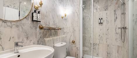 Un baño moderno con lavamanos de mármol, inodoro y ducha con cerramiento de vidrio.