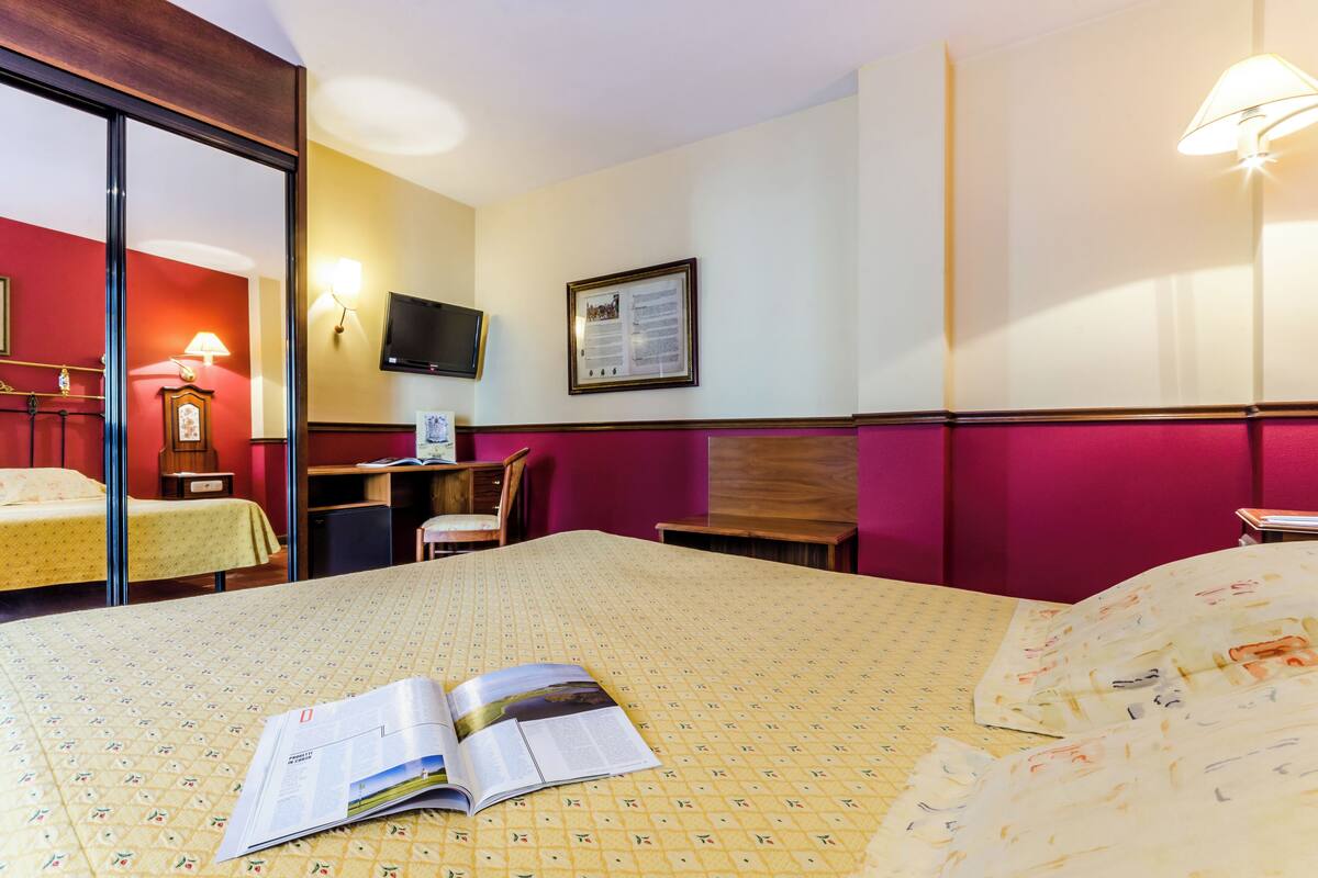 A hotel room with a bed, a desk, a chair, a television, and a framed picture on the wall.