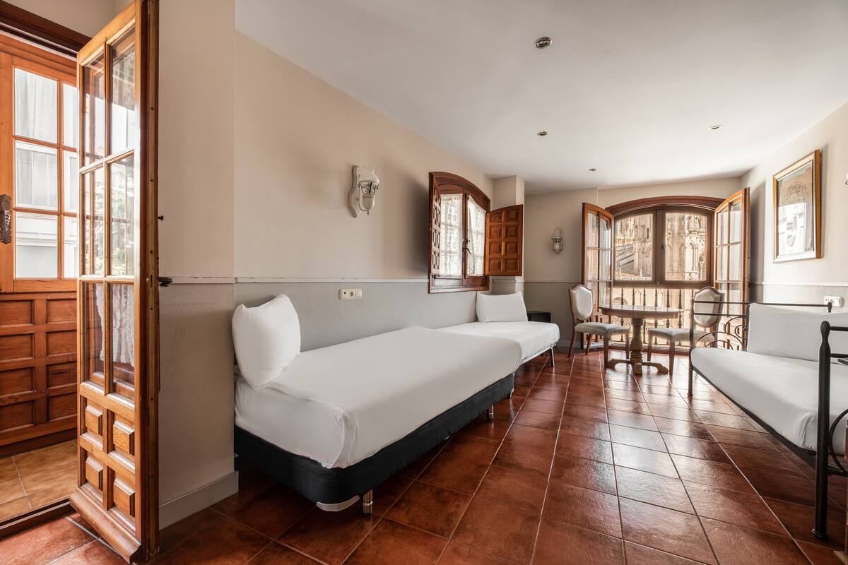 A room with two single beds, a dining table with chairs, and a large window with a view.