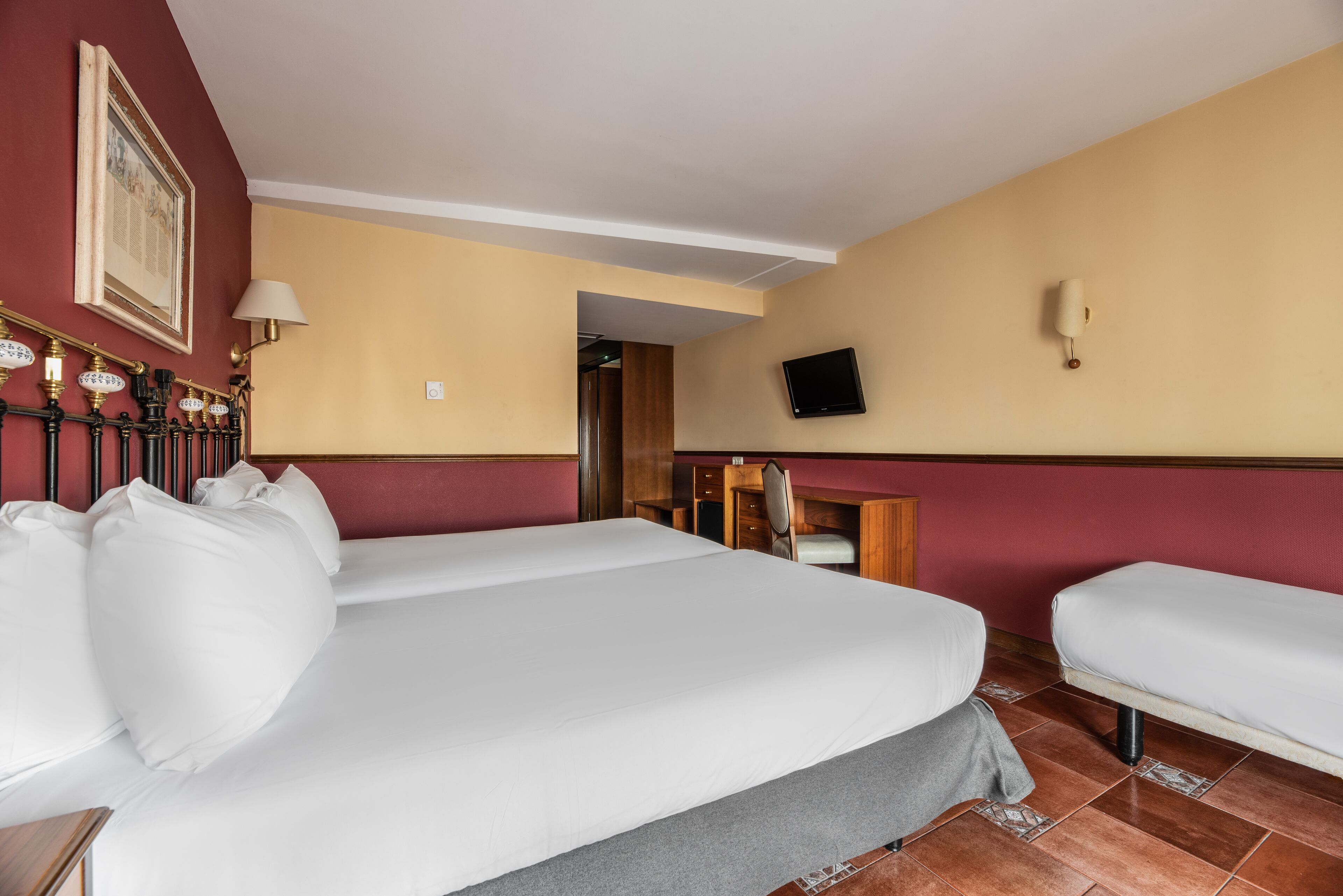 Ein Hotelzimmer mit einem großen Bett, einem Schreibtisch, einem Sessel und einem Fernseher an der Wand.