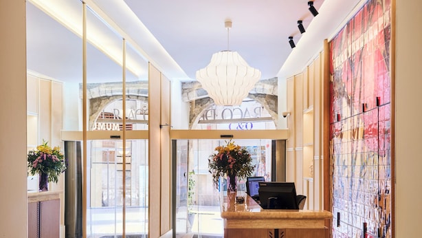 A hotel lobby with a reception desk, patterned floor tiles, and a large arched doorway leading to the entrance. - H10 Racó del Pi Boutique Hotel (Barcelona)