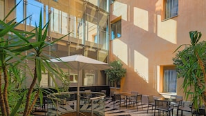 A modern building with a glass atrium, outdoor seating area, and potted plants. - H10 Racó del Pi Boutique Hotel (Barcelona)