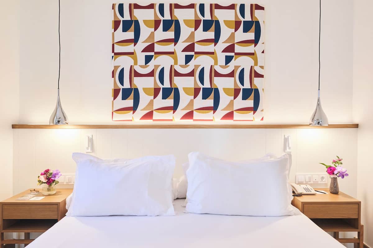 Una habitación de hotel con una cama, dos mesitas de noche, una obra de arte abstracta en la pared y un cabecero de madera.
