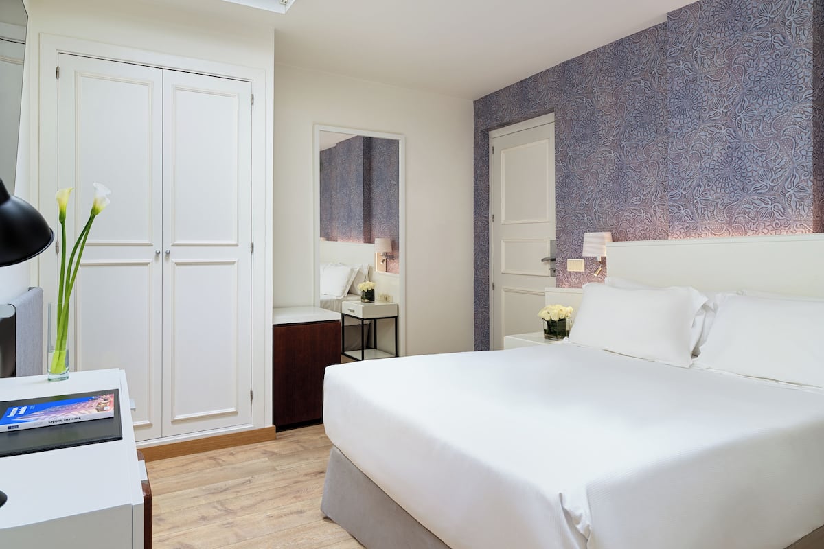 Una habitación de hotel con una cama grande, un escritorio con lámpara, un armario y un espejo.