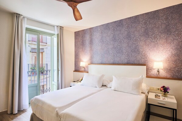 Habitación de hotel con dos camas, un balcón, papel tapiz estampado y un ventilador de techo.