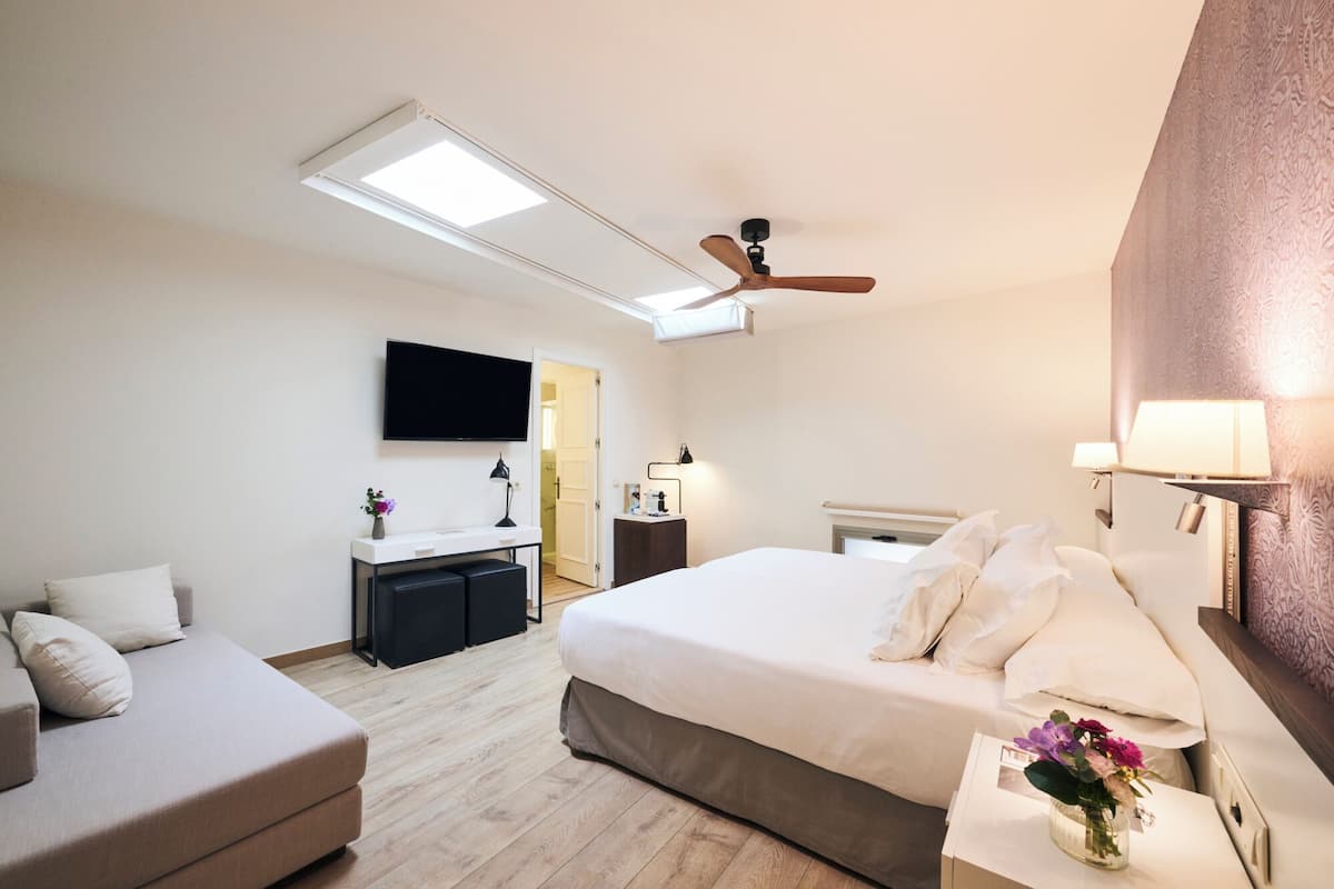 Una habitación de hotel con cama, escritorio, televisión, ventilador de techo y ventana.