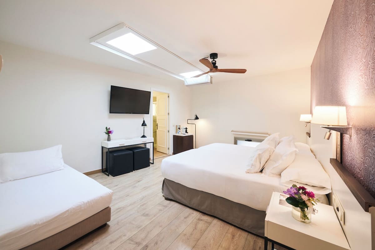 Habitación de hotel con cama, escritorio, televisor, ventilador de techo y ventana.