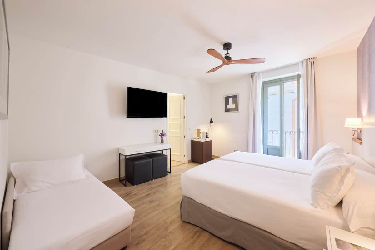 Habitación de hotel con dos camas, un escritorio, un televisor, un ventilador de techo y una ventana con cortinas.