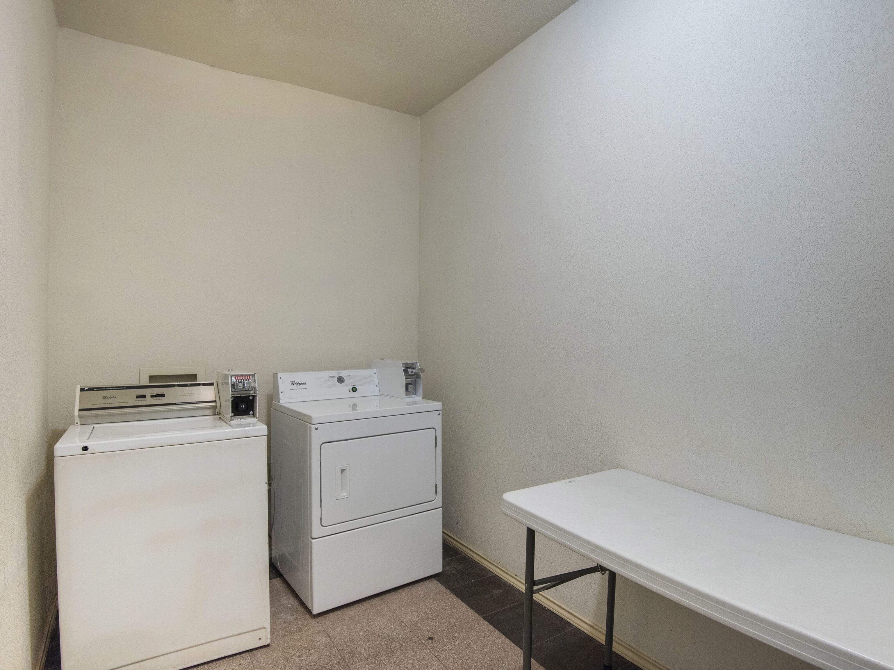 A laundry room with two stacked washers and dryers, a small table, and a plain wall.