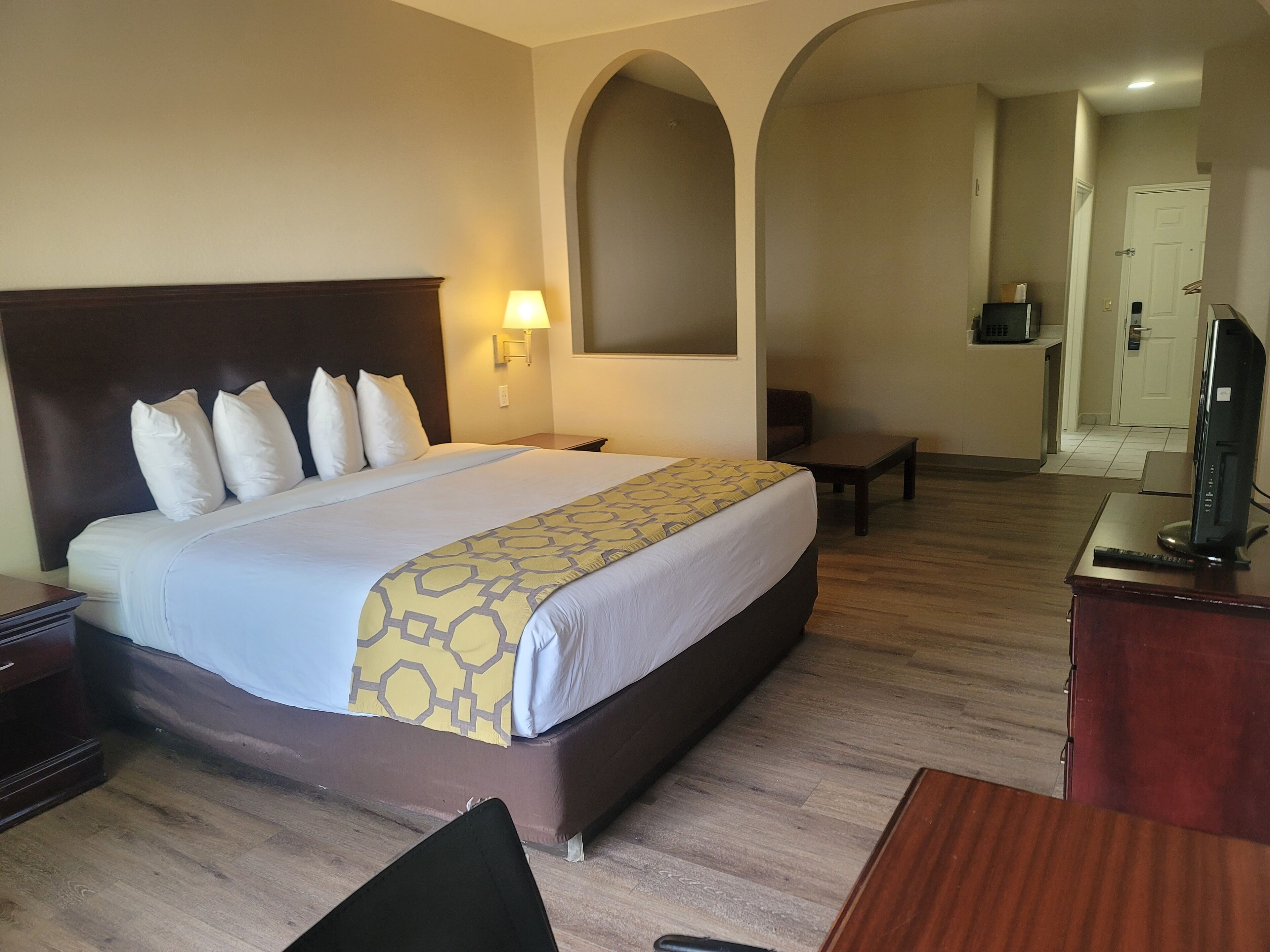 A hotel room with a large bed, a desk, a chair, a TV, and a small table.