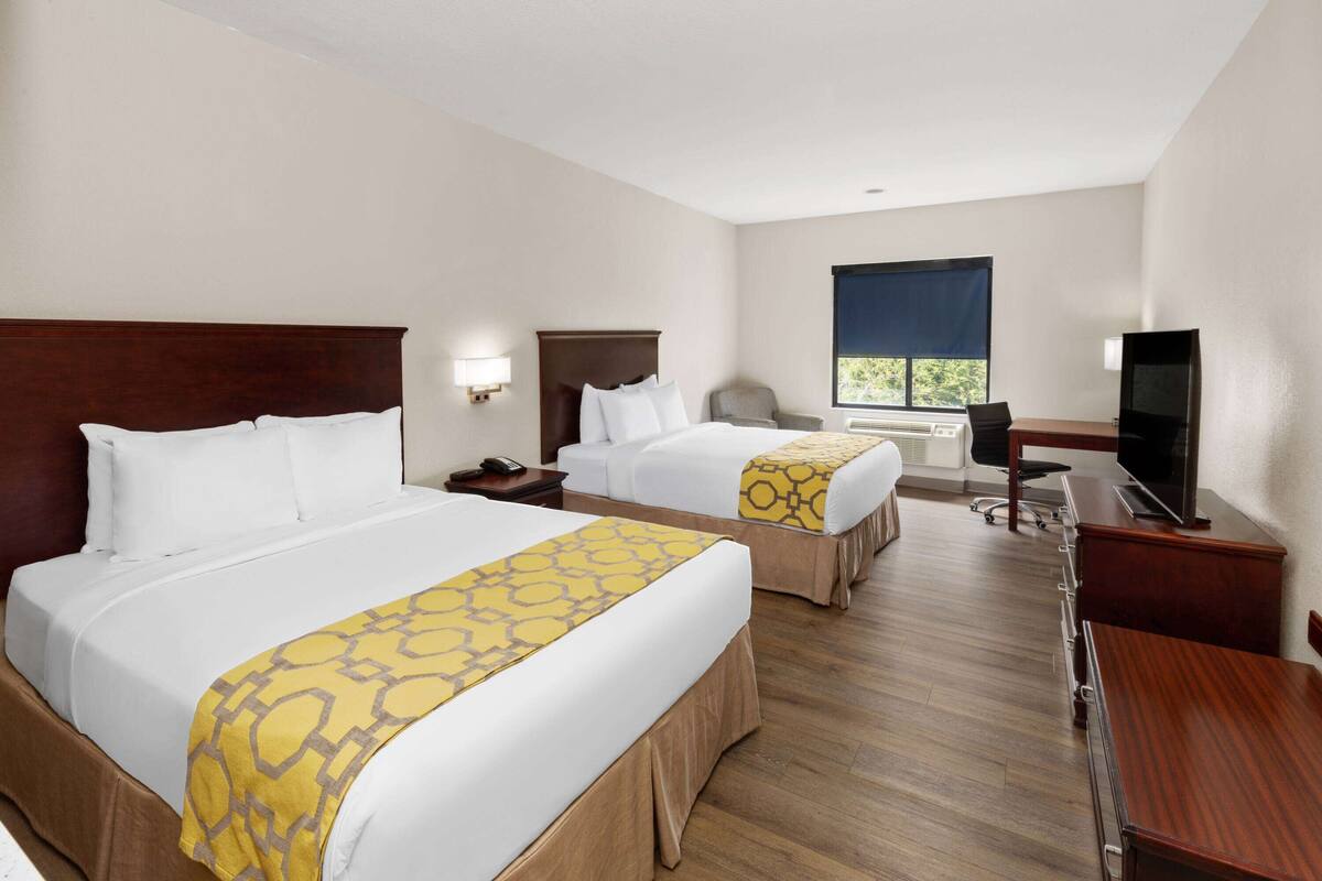 Una habitación de hotel con dos camas, un escritorio con televisor y una ventana con vistas.