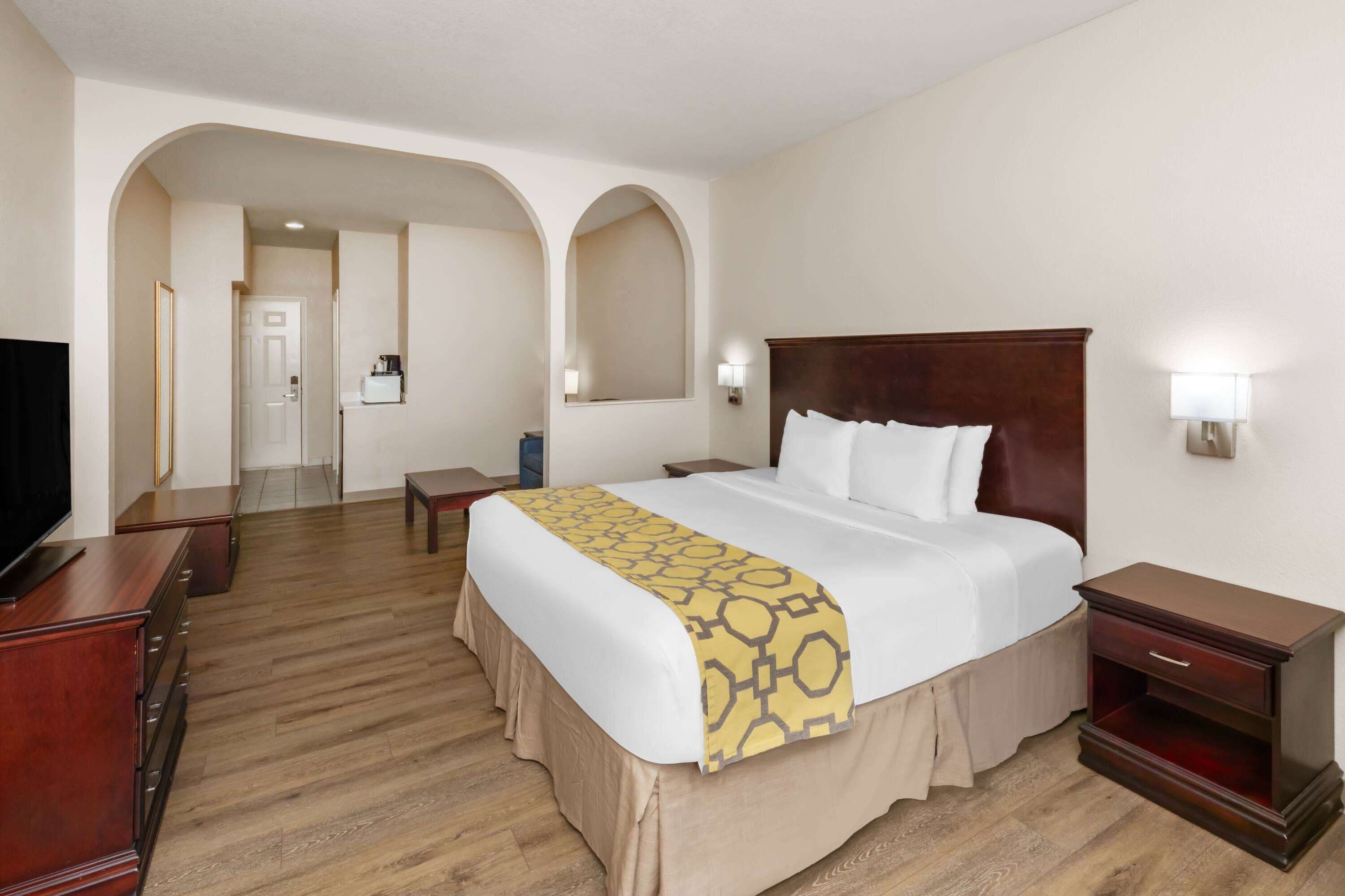 A hotel room with a large bed, wooden floor, a TV, a desk, and a nightstand.