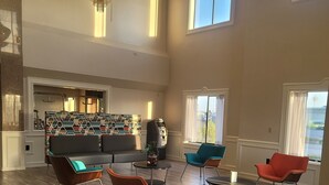 A spacious room with a high ceiling, a chandelier, and a seating area with modern chairs and a sofa. - Baymont by Wyndham Houston Brookhollow (Houston)