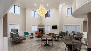 A spacious dining area with multiple tables and chairs, a chandelier, and a fireplace. - Baymont by Wyndham Houston Brookhollow (Houston)