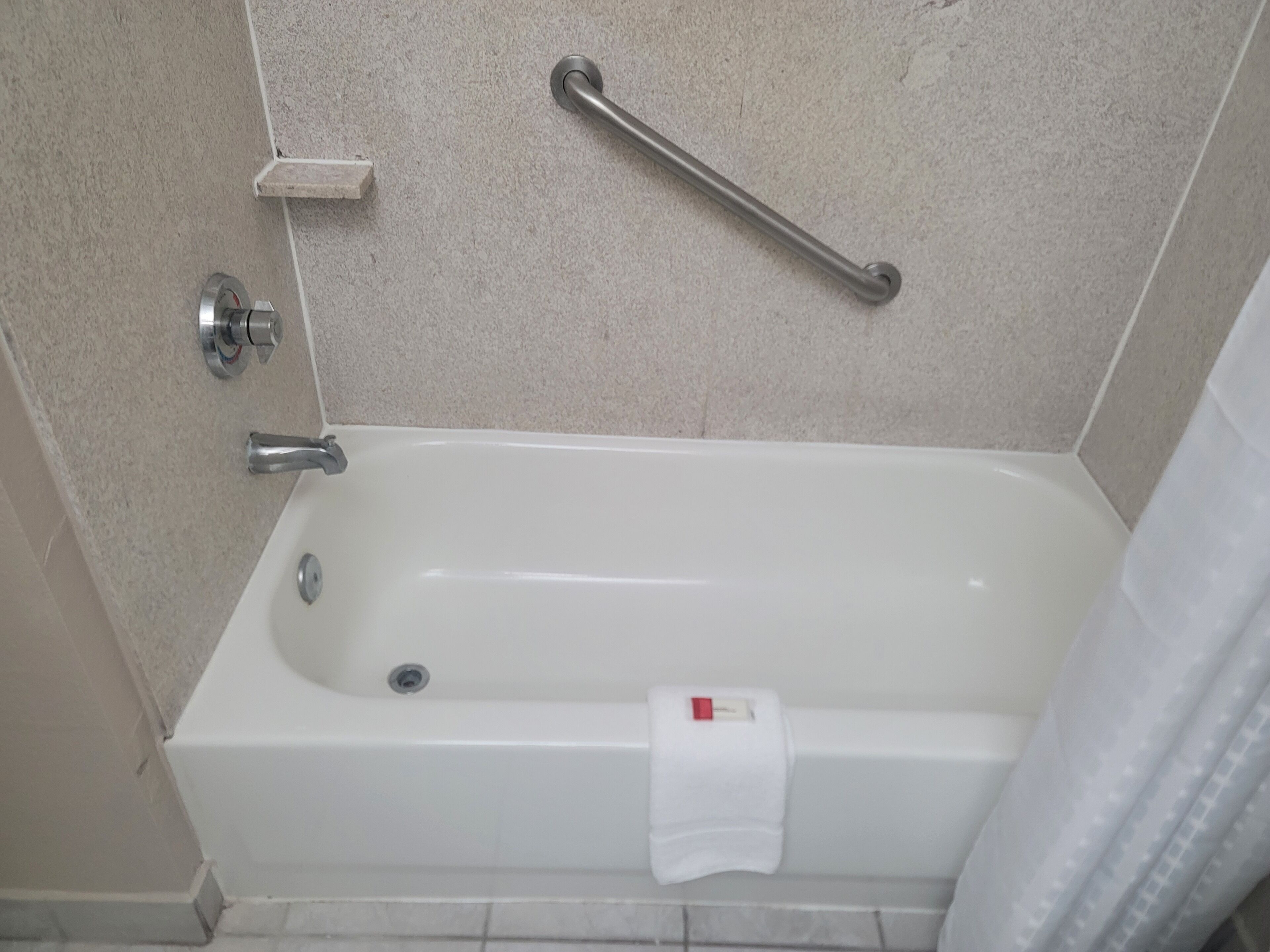 A bathroom with a bathtub, a handrail, a towel, and a soap dish.