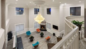 A spacious living area with a fireplace, comfortable seating, and a chandelier. - Baymont by Wyndham Houston Brookhollow (Houston)
