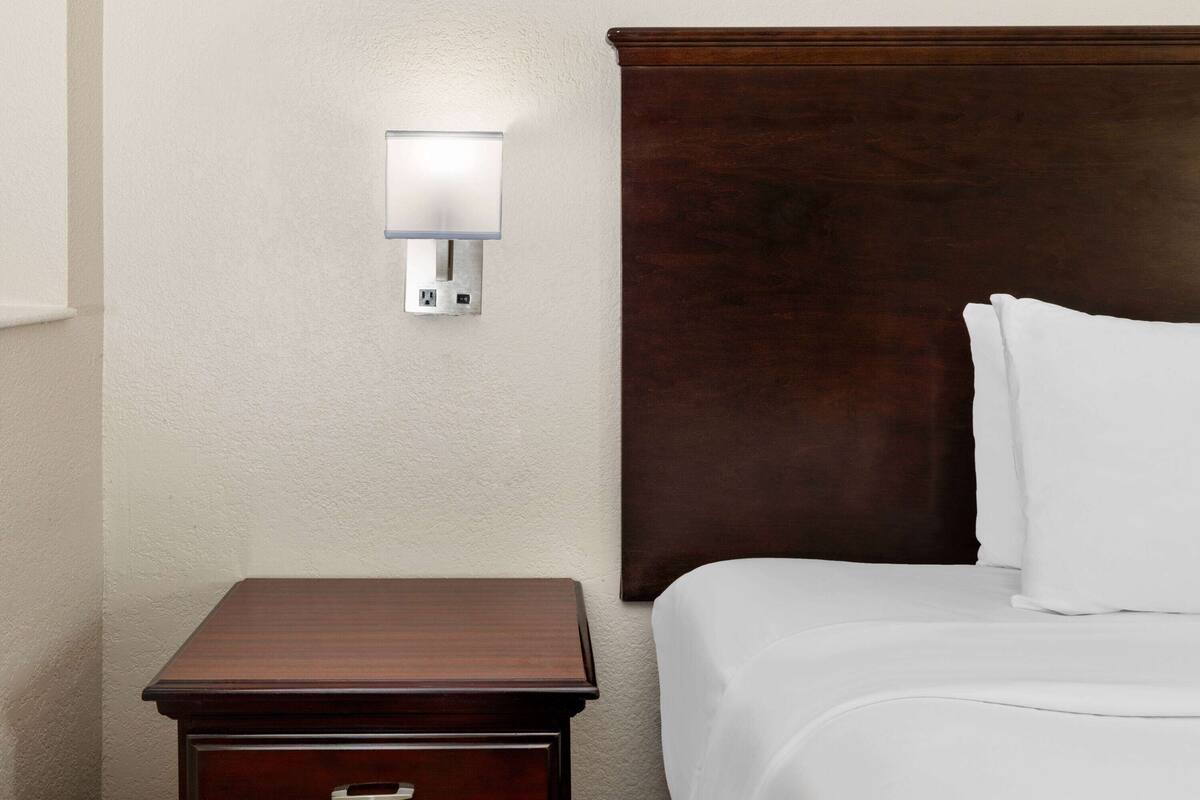 Habitación de hotel con cabecera de madera, mesita de noche con cajón y lámpara de pared.
