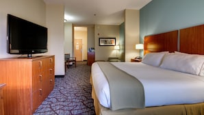 A hotel room with a large bed, a television on a wooden dresser, a desk with a lamp, and a carpeted floor. - Holiday Inn Express Hotel & Suites Jacksonville South I-295 by IHG (Jacksonville)