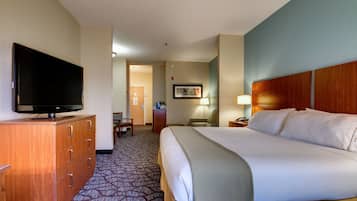 A hotel room with a large bed, a television on a wooden dresser, a desk with a lamp, and a carpeted floor.