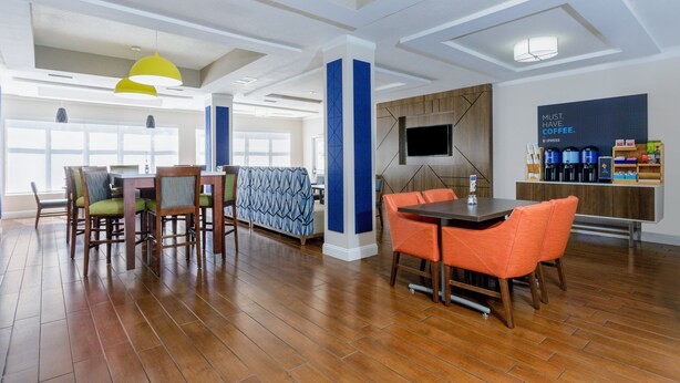 A spacious dining area with wooden flooring, a central table with orange chairs, and a seating area with patterned cushions.