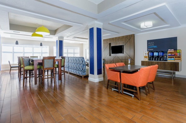 A spacious dining area with wooden flooring, a central table with orange chairs, and a seating area with patterned cushions.