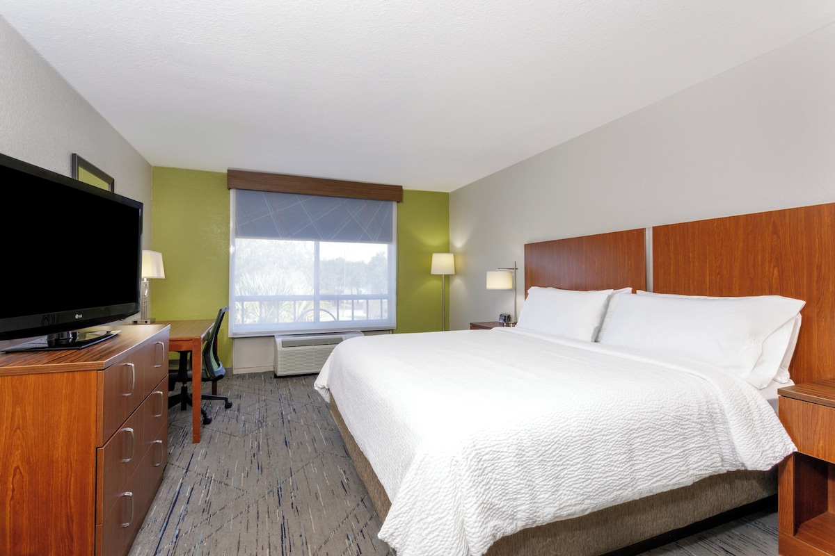 A hotel room with a bed, a desk, a television, and a window with blinds.
