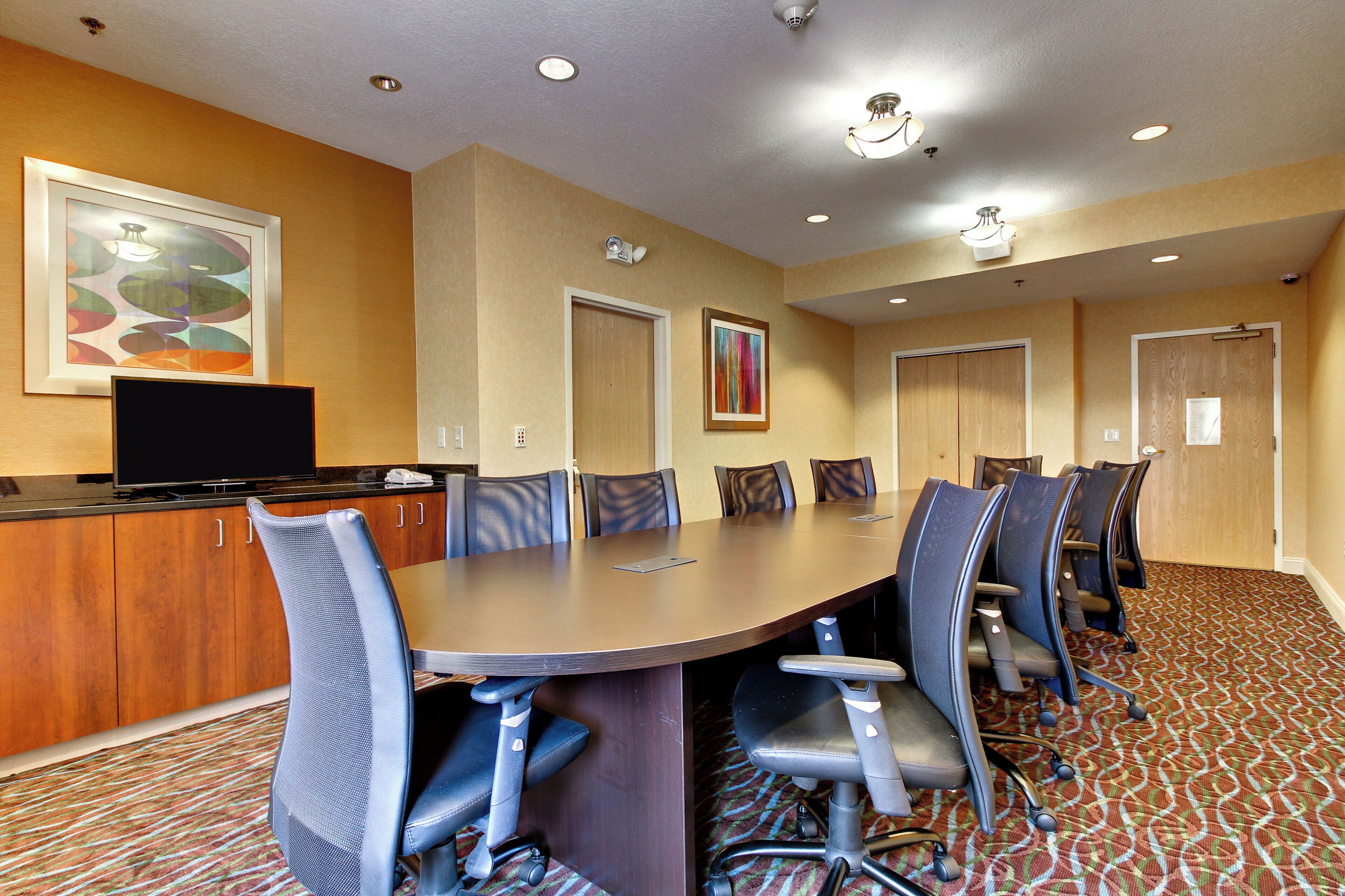 A conference room with a long table, chairs, a television, and artwork on the walls.