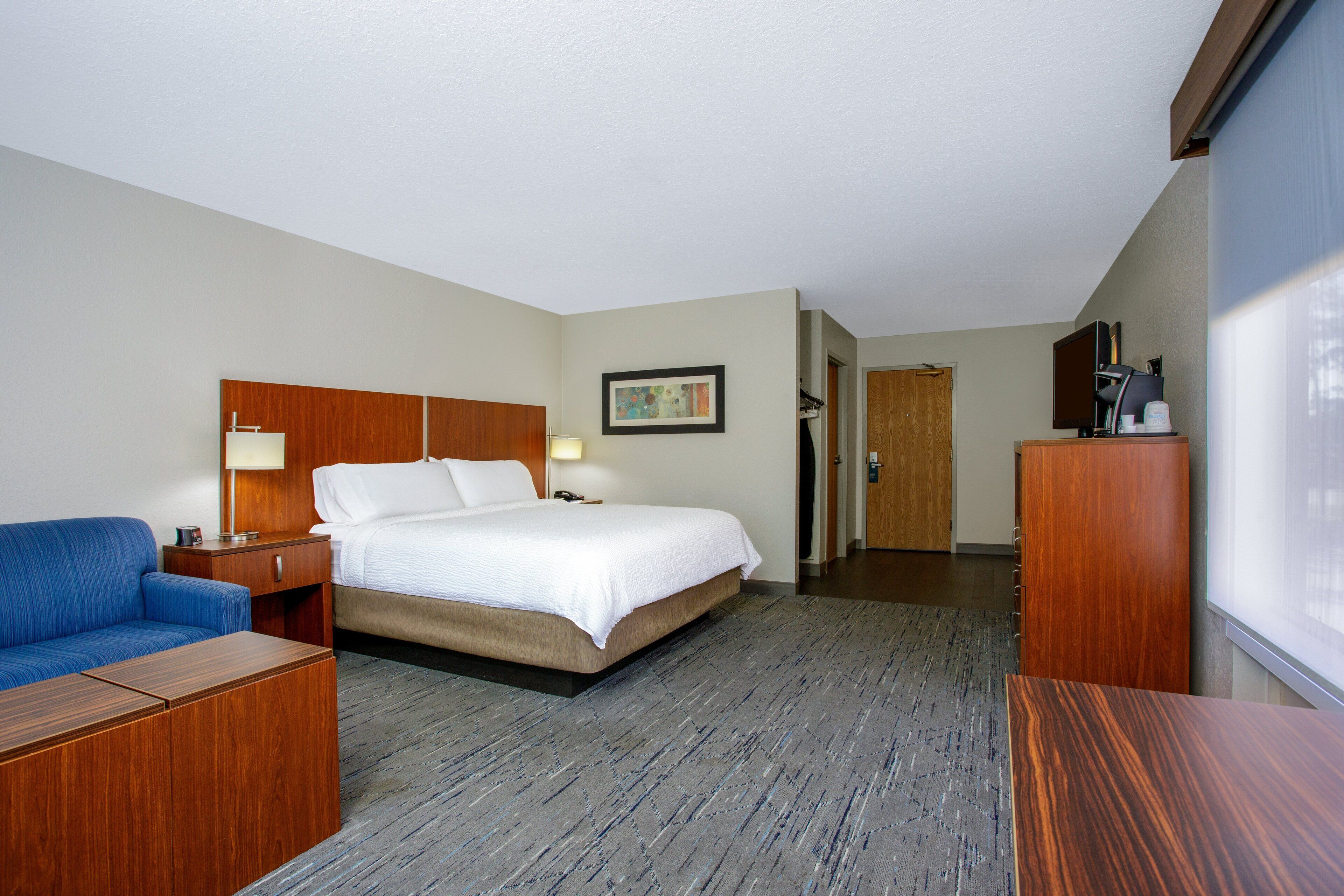 Habitación de hotel con cama, escritorio, silla, armario y televisor.