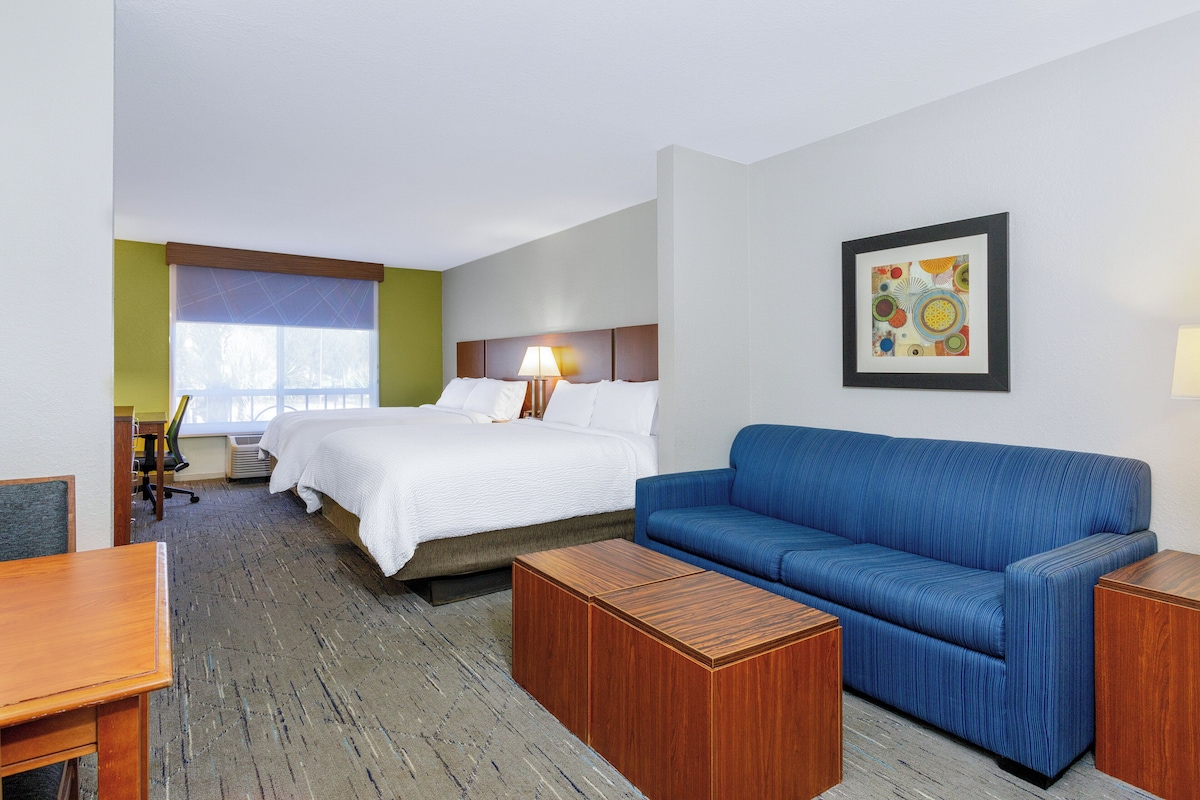 A hotel room with a bed, a blue sofa, a wooden coffee table, a desk, and a picture on the wall.