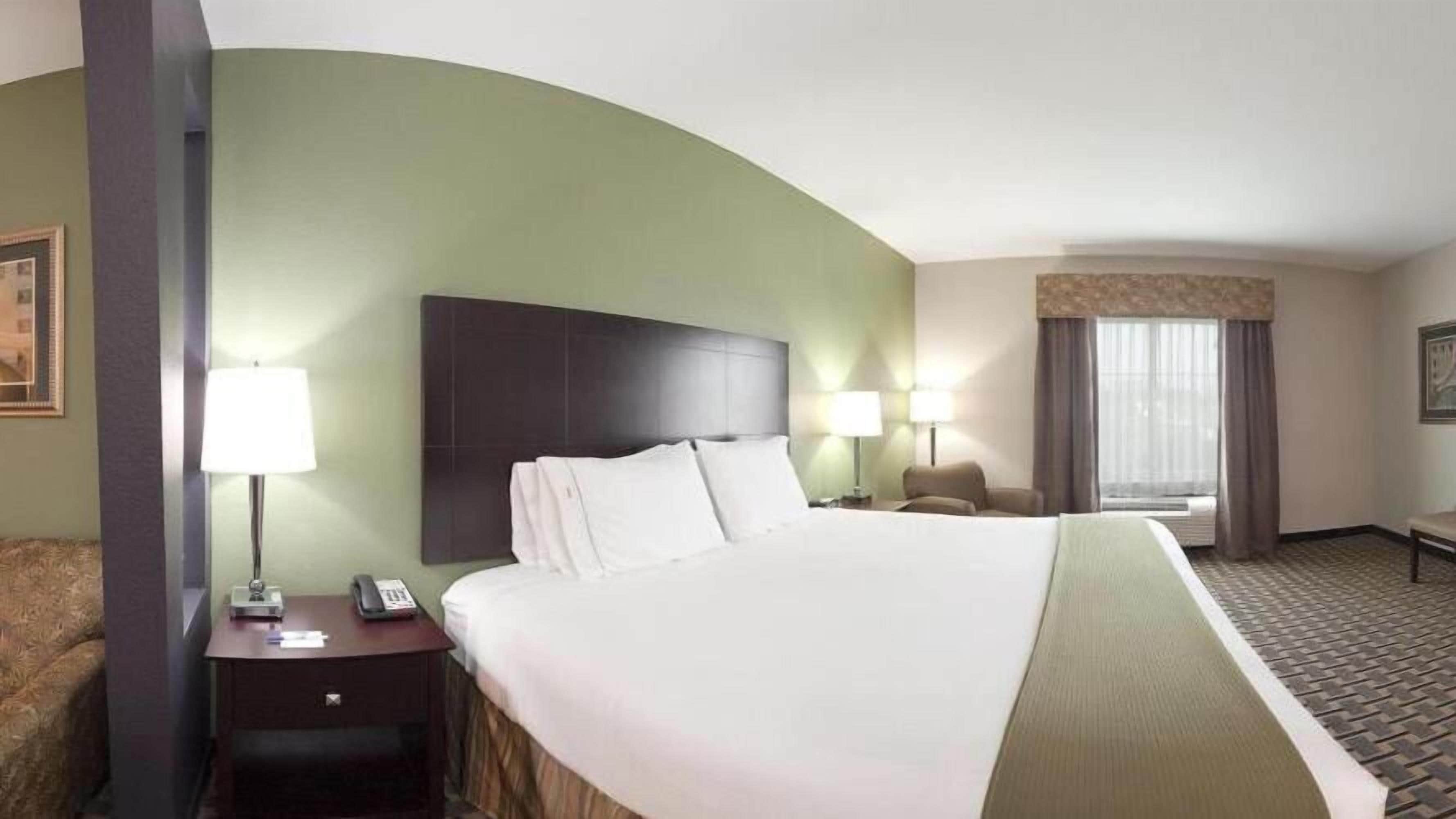 A hotel room with a large bed, two bedside lamps, a nightstand, a chair, and a window with curtains.