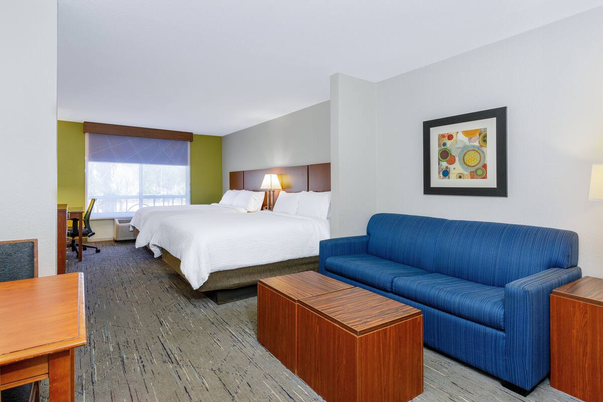 Ein Hotelzimmer mit einem Bett, einem blauen Sofa, einem Holztisch, einem Schreibtisch und einem Bild an der Wand.