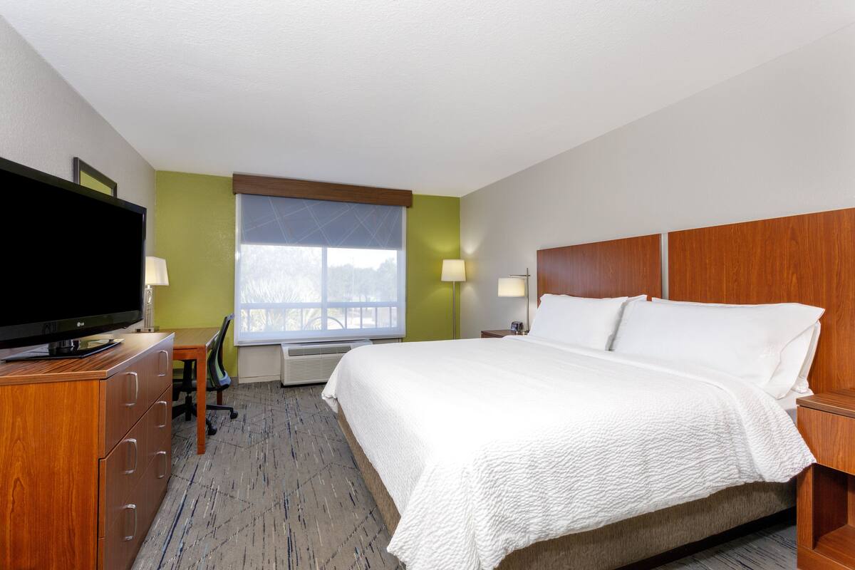 Ein Hotelzimmer mit Bett, Schreibtisch, Fernseher und einem Fenster mit Jalousien.