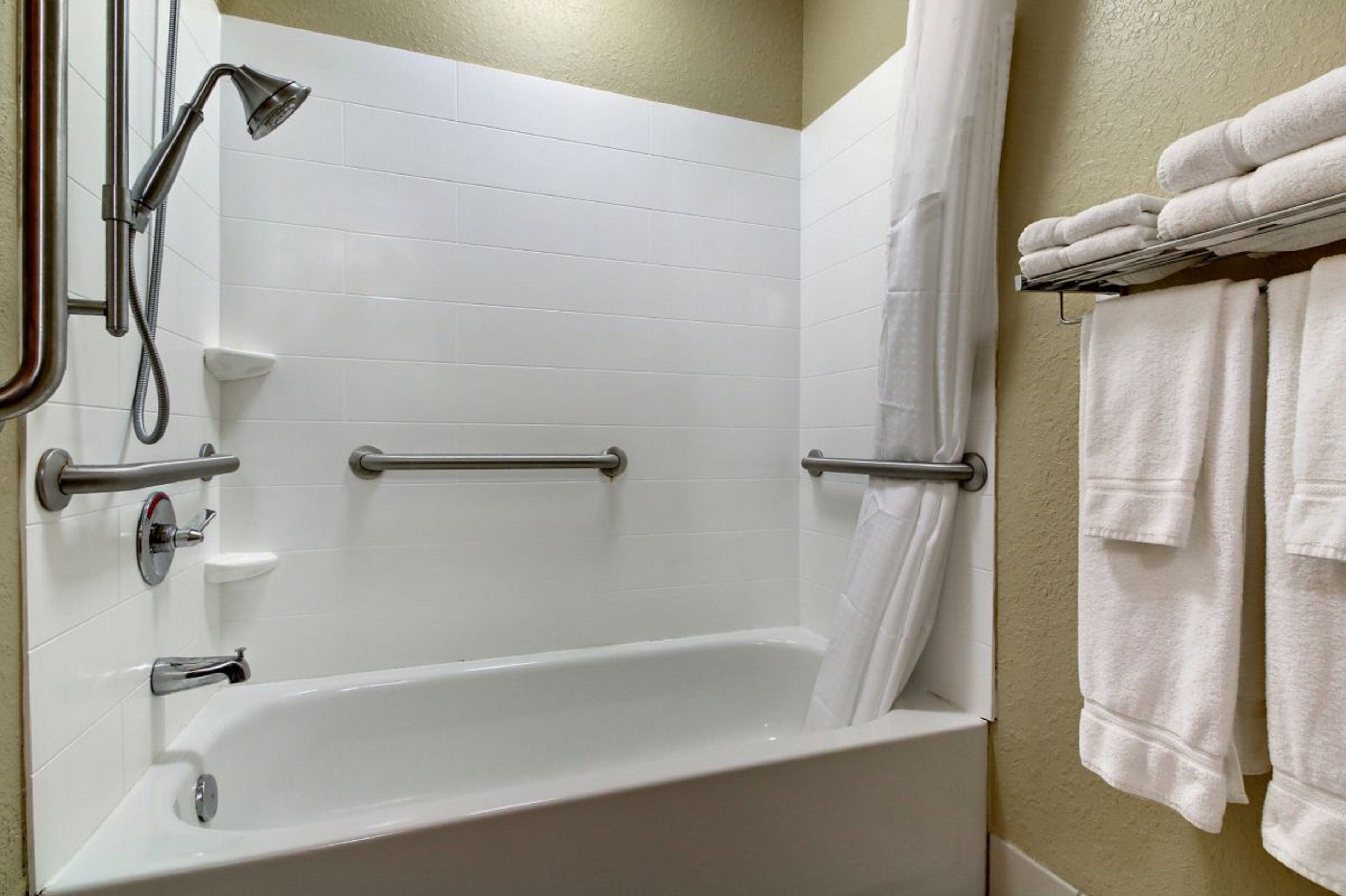 Une salle de bain avec une baignoire blanche, des barres d’appui, une pomme de douche et un porte-serviettes avec des serviettes.