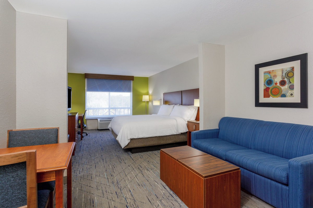 A hotel room with a bed, a blue sofa, a wooden table, a desk, and a window with a view.