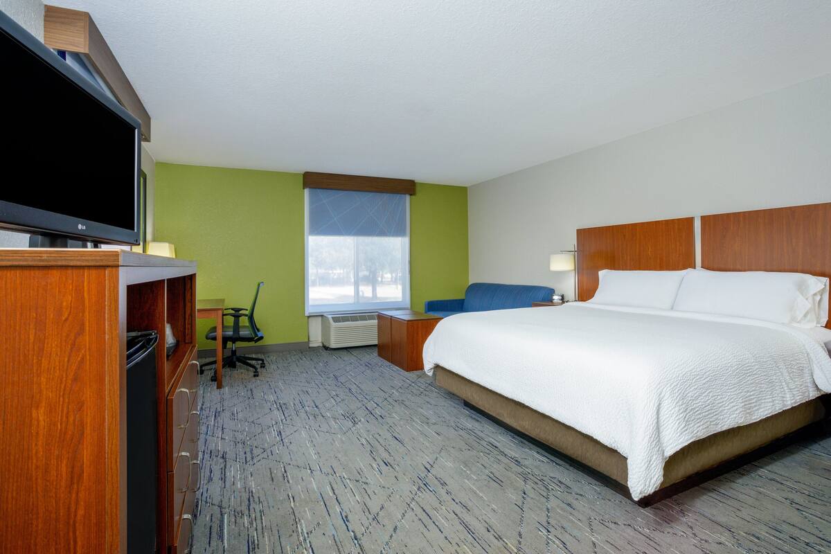 Ein Hotelzimmer mit Bett, Schreibtisch, Stuhl, Fernseher und Fenster.