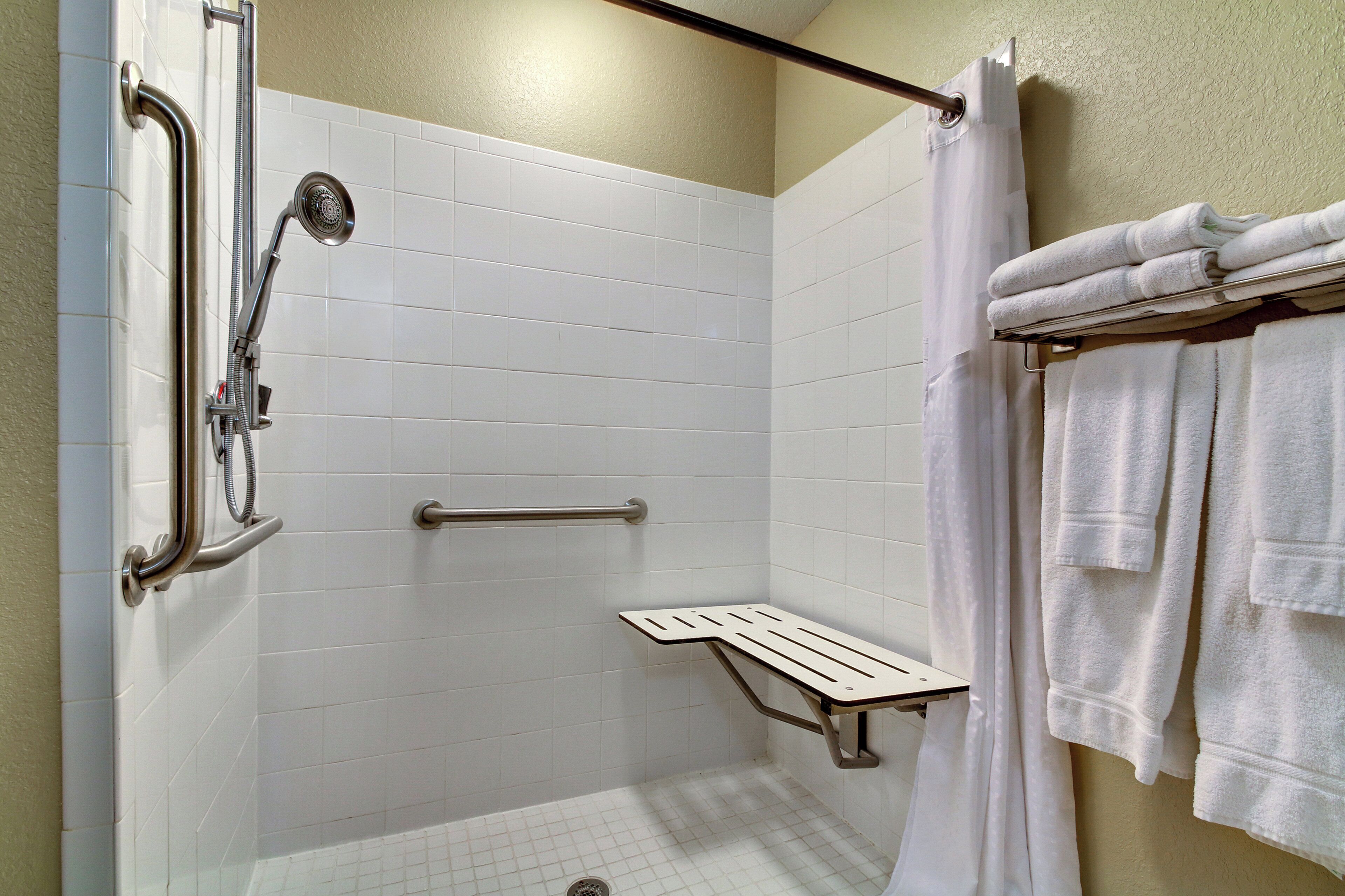 A shower area with a grab bar, a towel rack, and a shower seat.