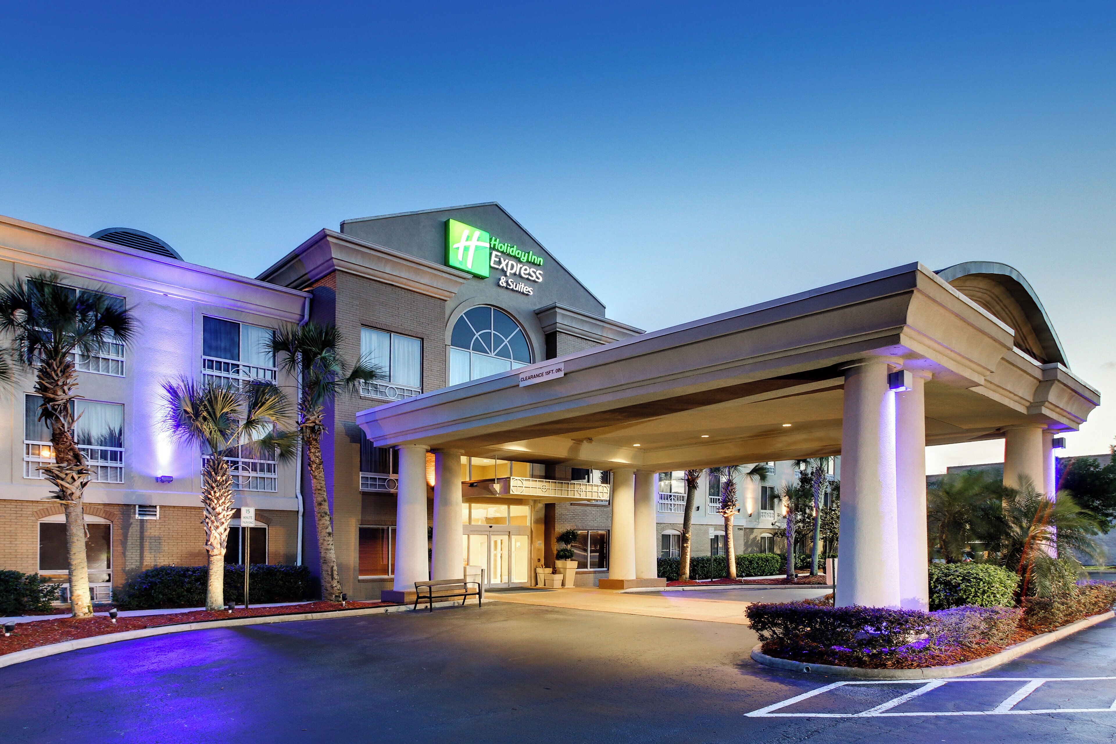 Um Holiday Inn Express & Suites com entrada coberta, palmeiras e estacionamento.