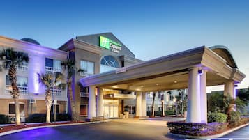 A Holiday Inn Express & Suites with a covered entrance, palm trees, and a parking lot.