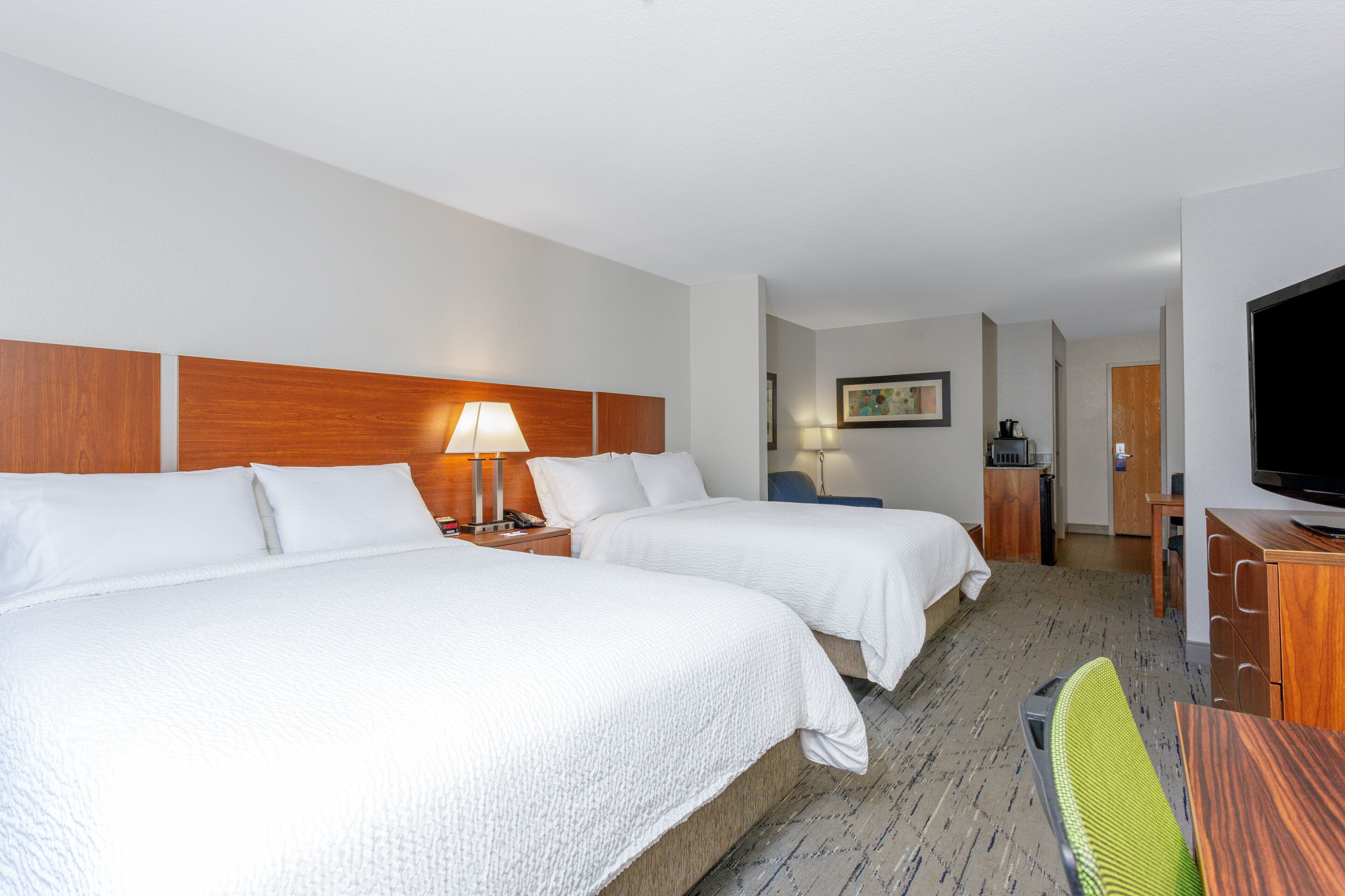 A hotel room with two beds, a desk, a chair, a television, and a bathroom visible in the background.